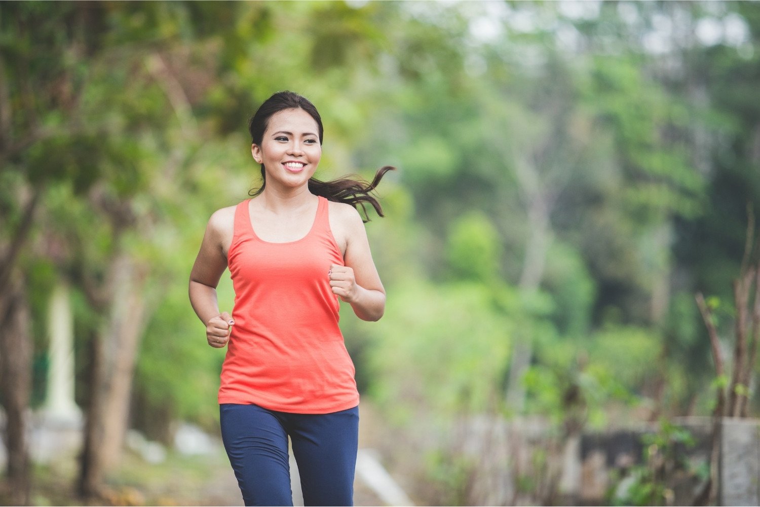 Woman jogging on paved path in outdoor sunlight.