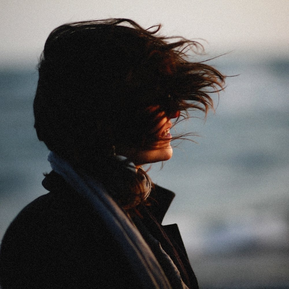 Woman standing by the sea with wind blowing through her hair, symbolizing change and personal growth.