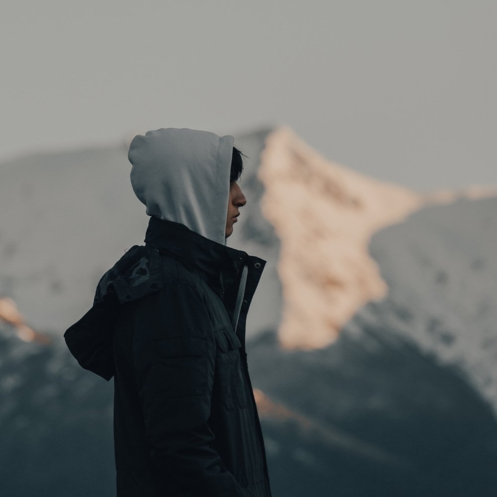 Man in a hooded jacket standing before snow-covered mountains symbolizing focus, solitude, and inner strength