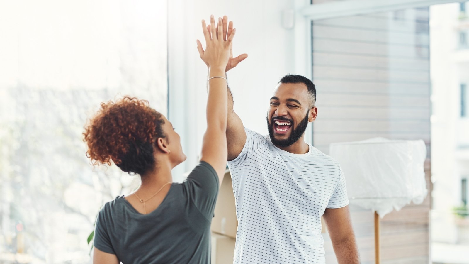 Two friends giving enthusiastic high-five celebrating success together in bright modern space